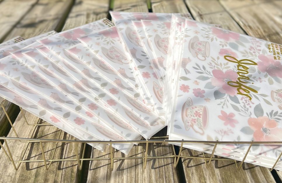Set of floral-patterned envelopes on a wooden surface with a metal stand.